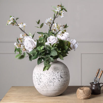 Decorative vase with flowers on a wooden surface against a gray wall