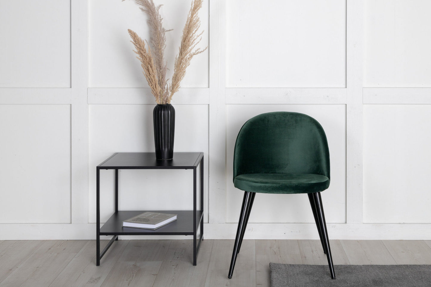 Green chair and black side table against a white paneled wall.