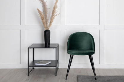 Green chair and black side table against a white paneled wall.