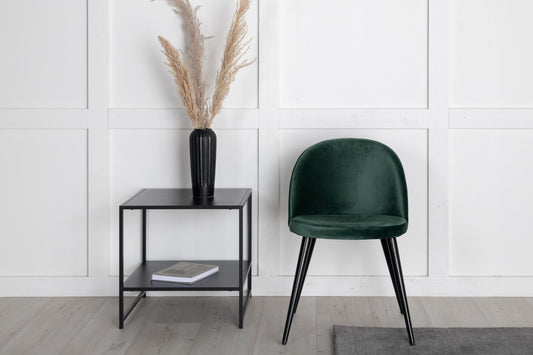 Green chair and black side table against a white paneled wall.