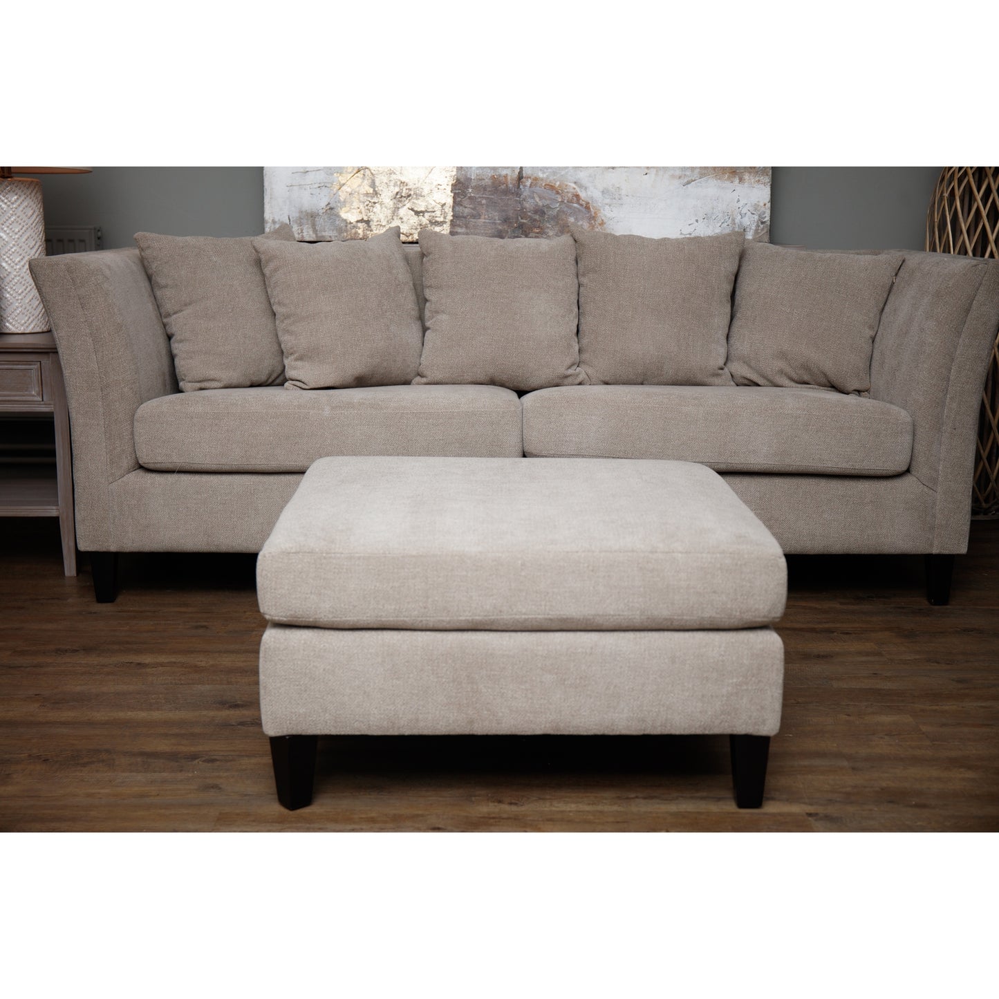 Beige sectional sofa with matching ottoman on a wooden floor.