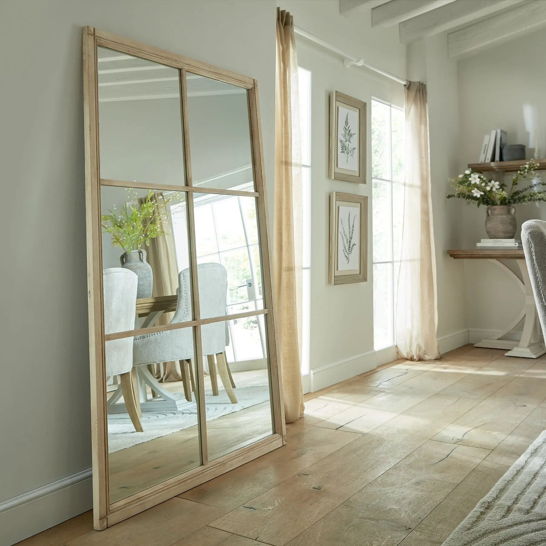 Large floor mirror with wooden frame in a room with light-colored walls and wooden flooring.