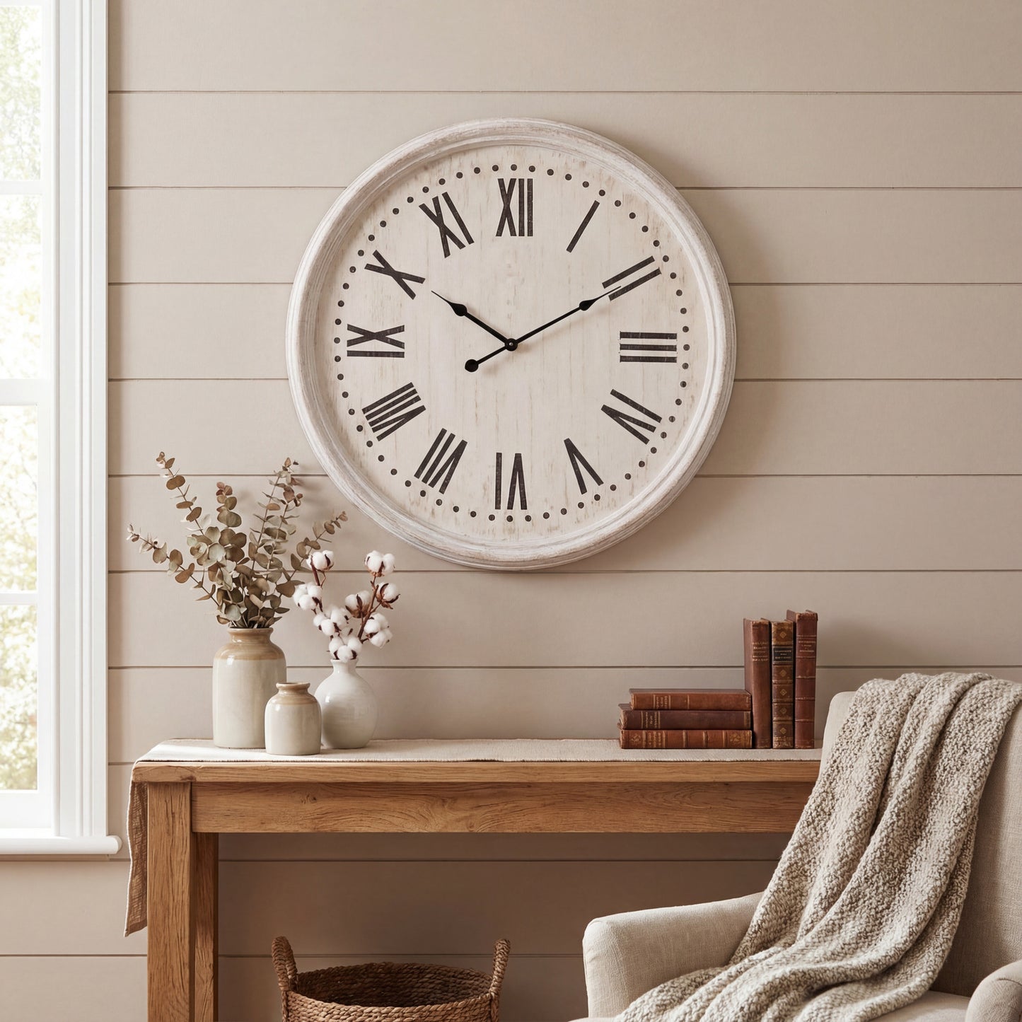 Large round wall clock on a neutral wall with a wooden desk and chair in the foreground.