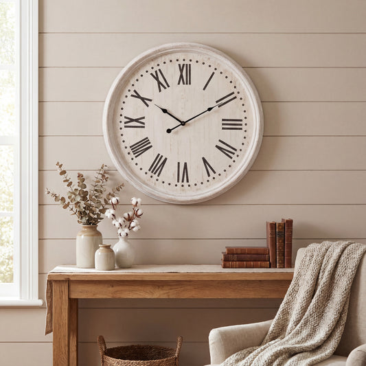 Large round wall clock on a neutral wall with a wooden desk and chair in the foreground.
