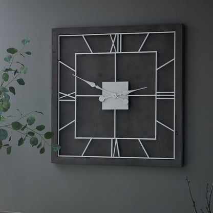 Geometric wall clock on a dark gray wall with a plant to the left.