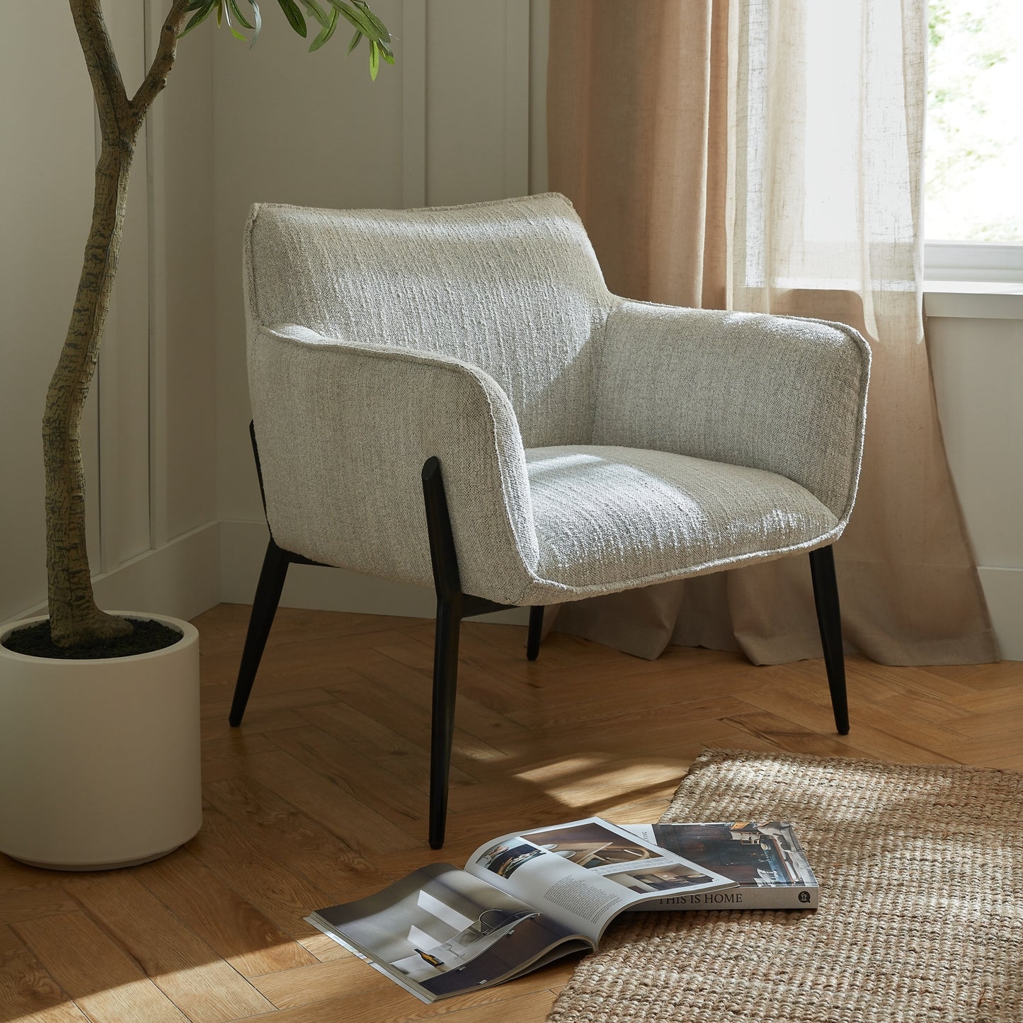 Modern armchair in a room with a plant, open magazine, and curtains.