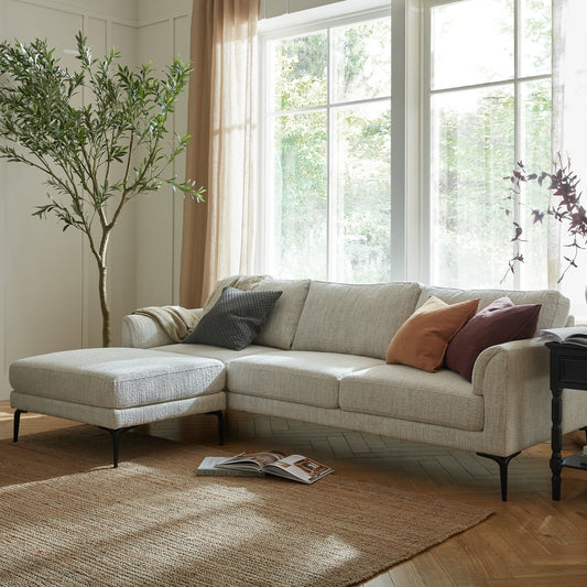 Beige sectional sofa with cushions in a bright living room with large windows.