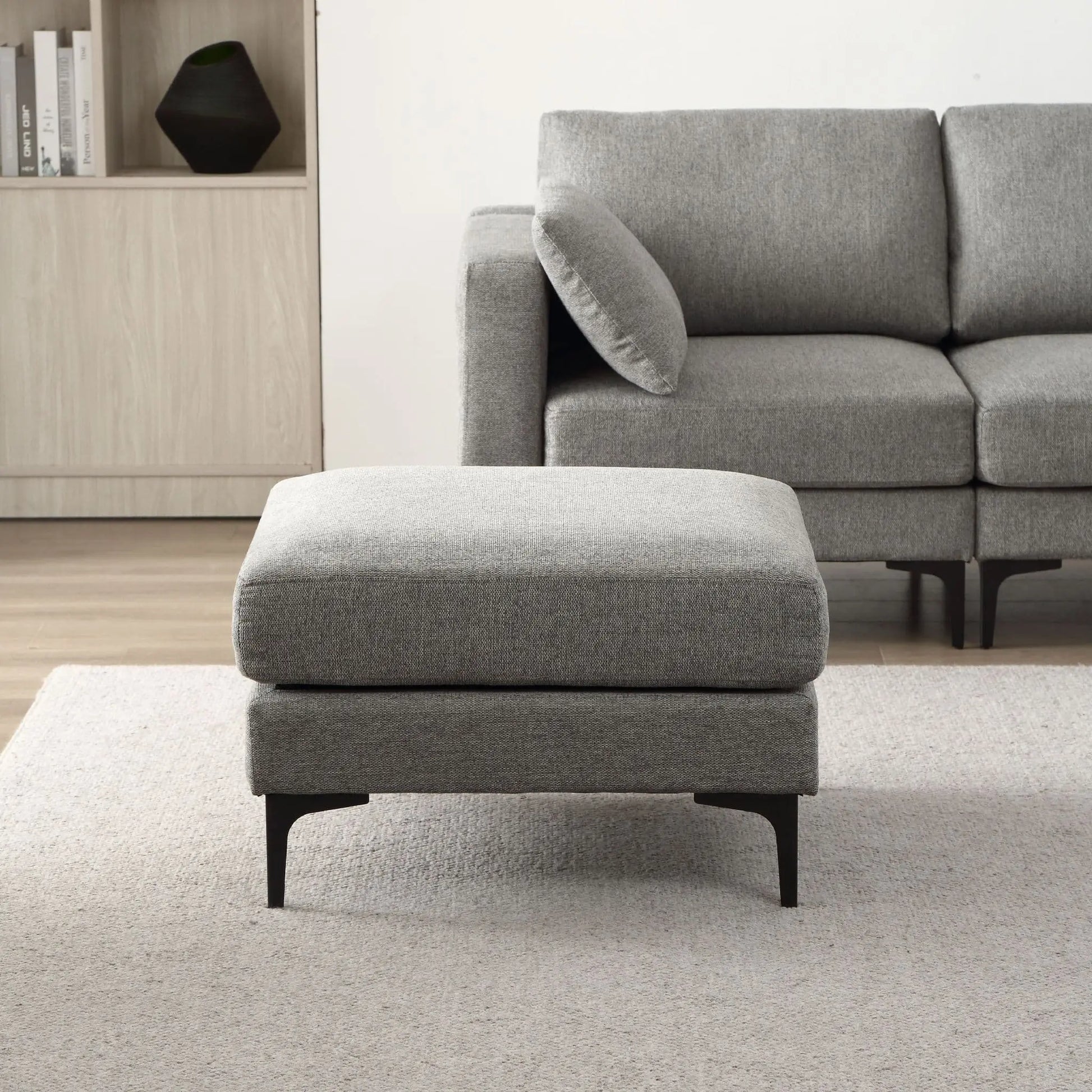 Gray upholstered ottoman in front of a gray sofa in a living room setting.