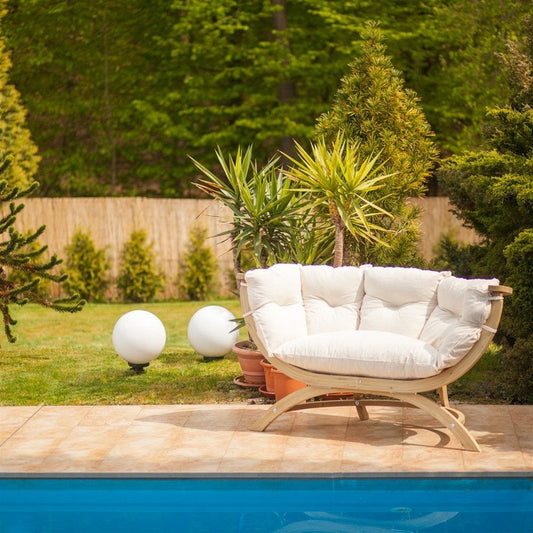 White outdoor sofa with cushions by a poolside in a garden setting