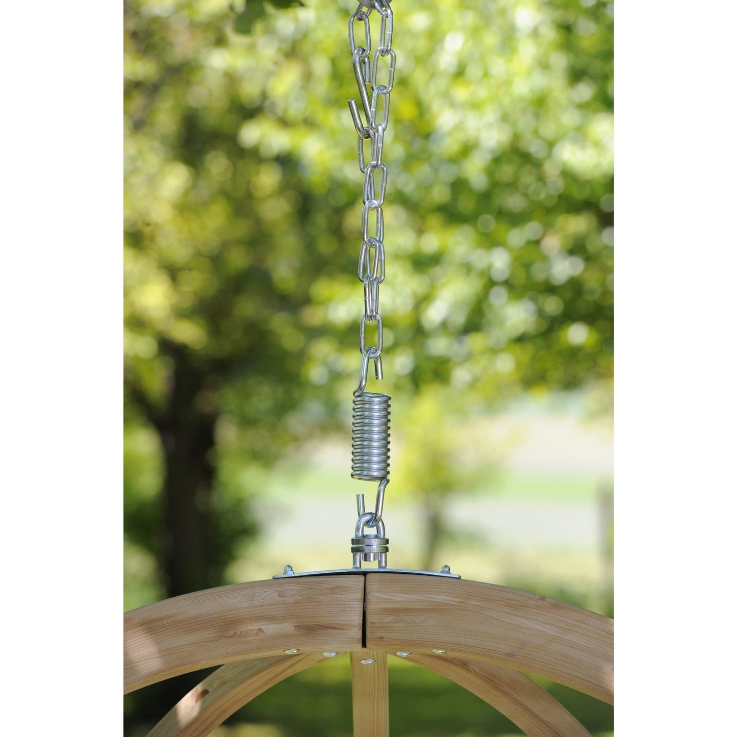 Wooden swing with metal chain and spring against a blurred green outdoor background