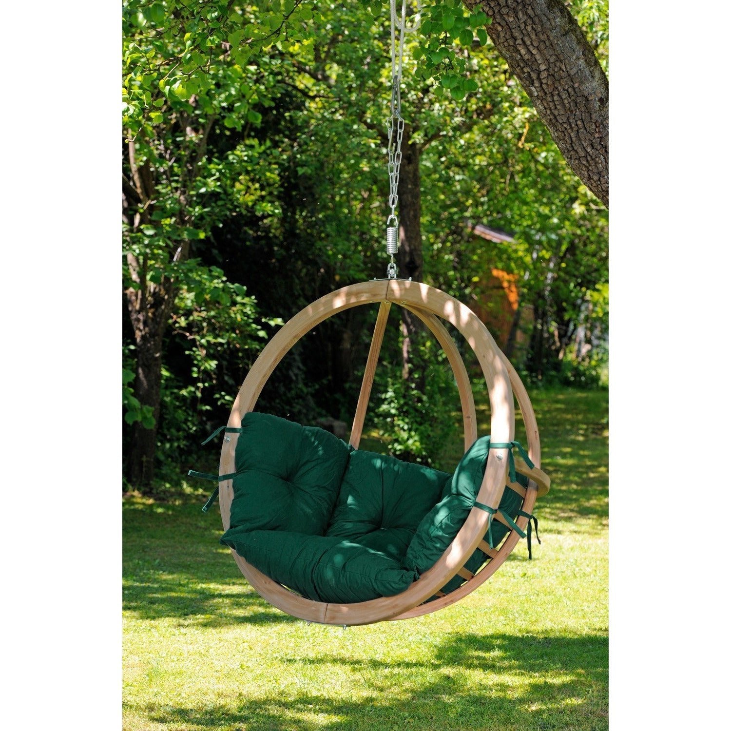 Hanging chair with green cushions hanging from a tree in a garden.