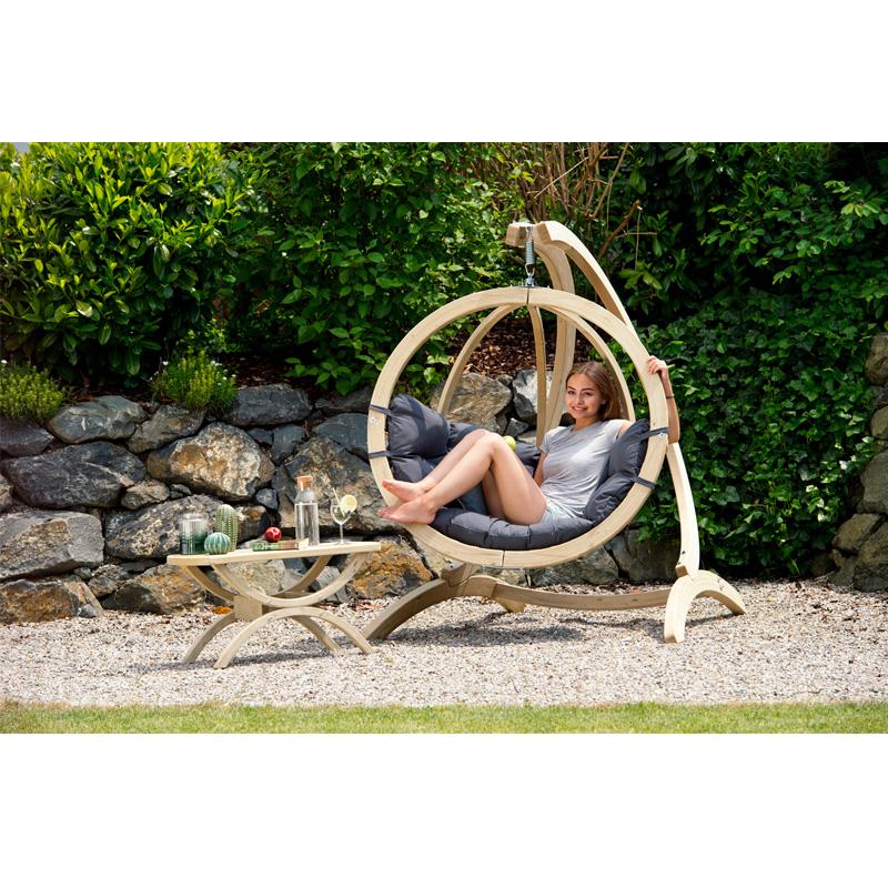 Person relaxing in a hanging chair with a small table in a garden setting.