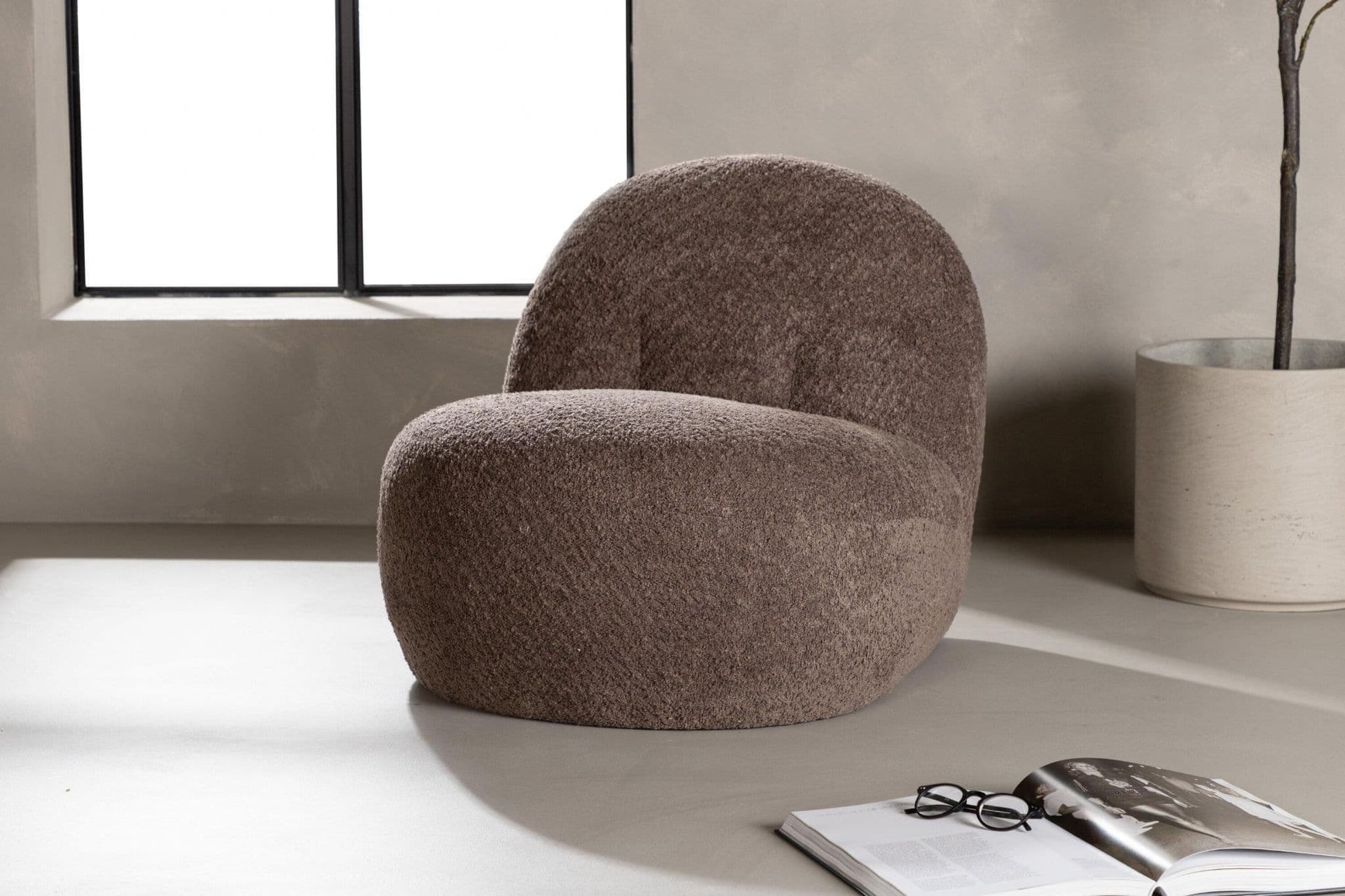 Brown textured armchair in a modern room with a window and plant.