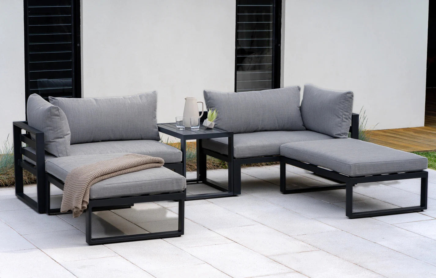 Outdoor patio furniture set with gray cushions on a white patio.