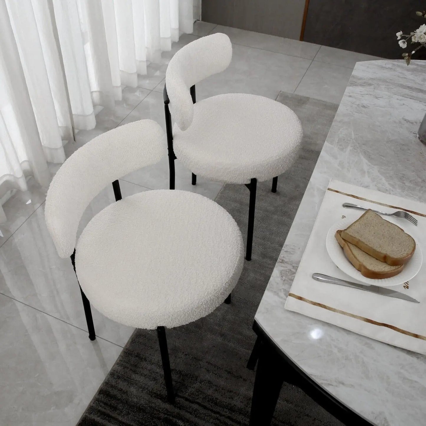 White cushioned chairs around a dining table with a plate of bread and cutlery.