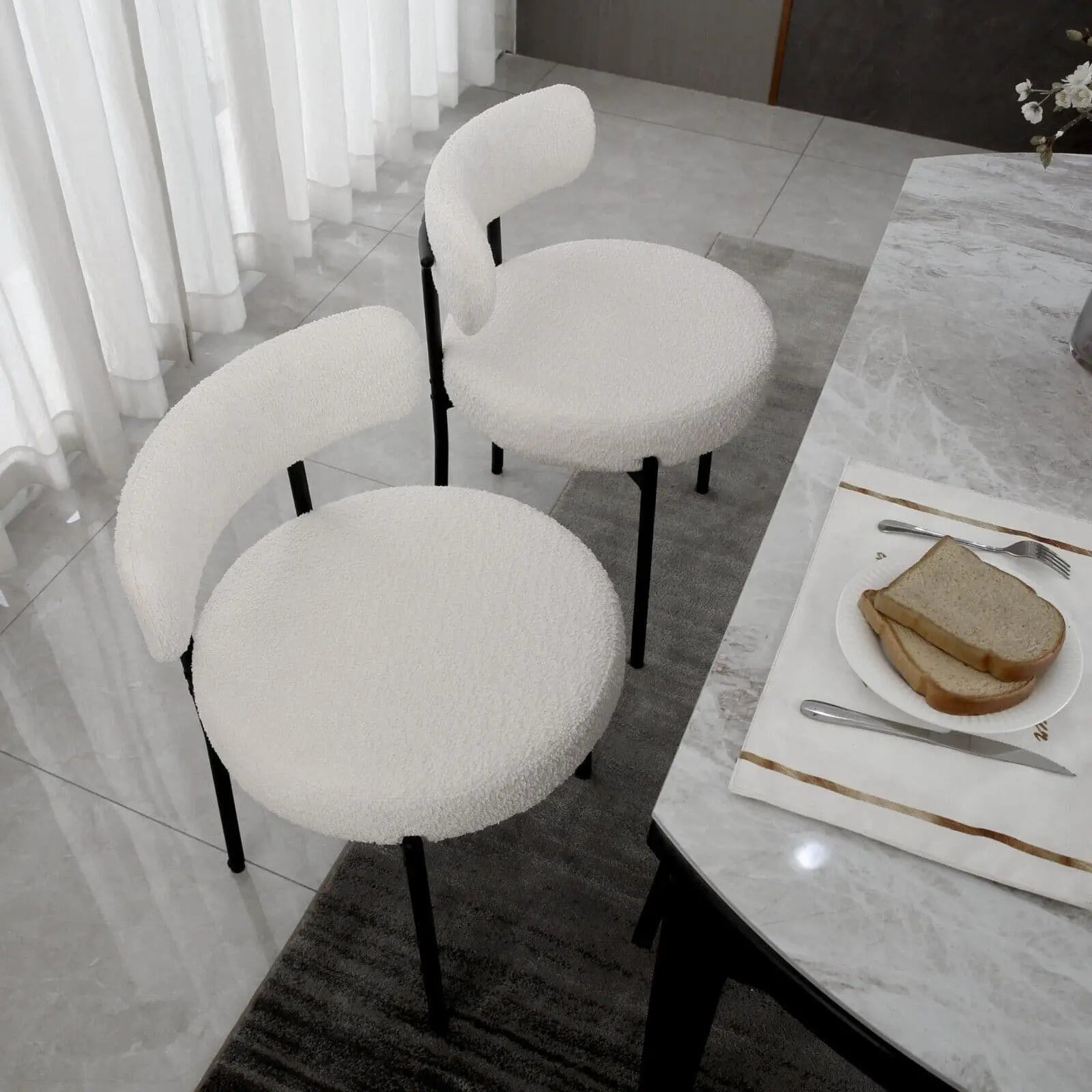 White cushioned chairs around a dining table with a plate of bread and cutlery.