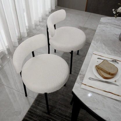 White cushioned chairs around a dining table with a plate of bread and cutlery.