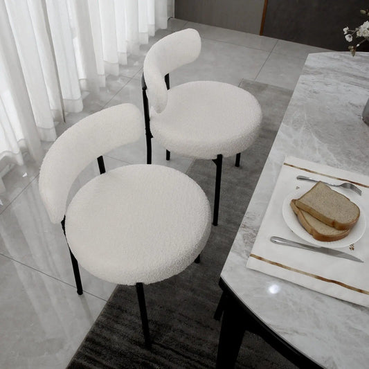 White cushioned chairs around a dining table with a plate of bread and cutlery.