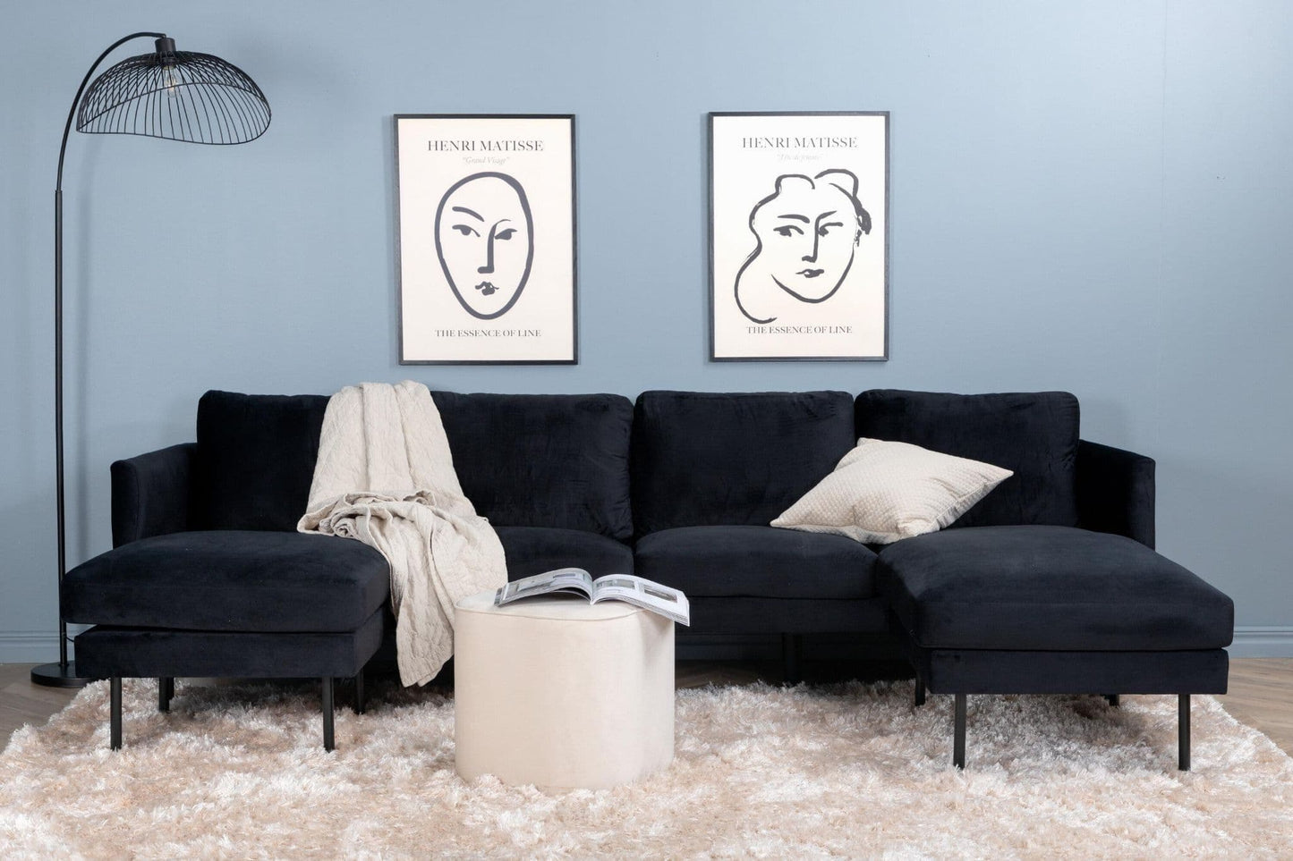 Black sectional sofa in a living room with two framed artworks on the wall.