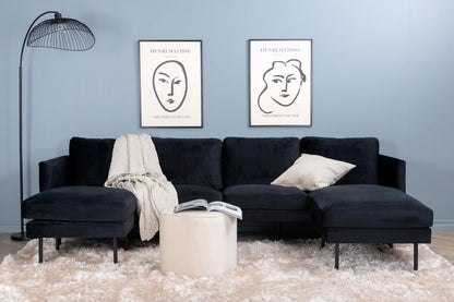 Black sectional sofa in a living room with two framed artworks on the wall.
