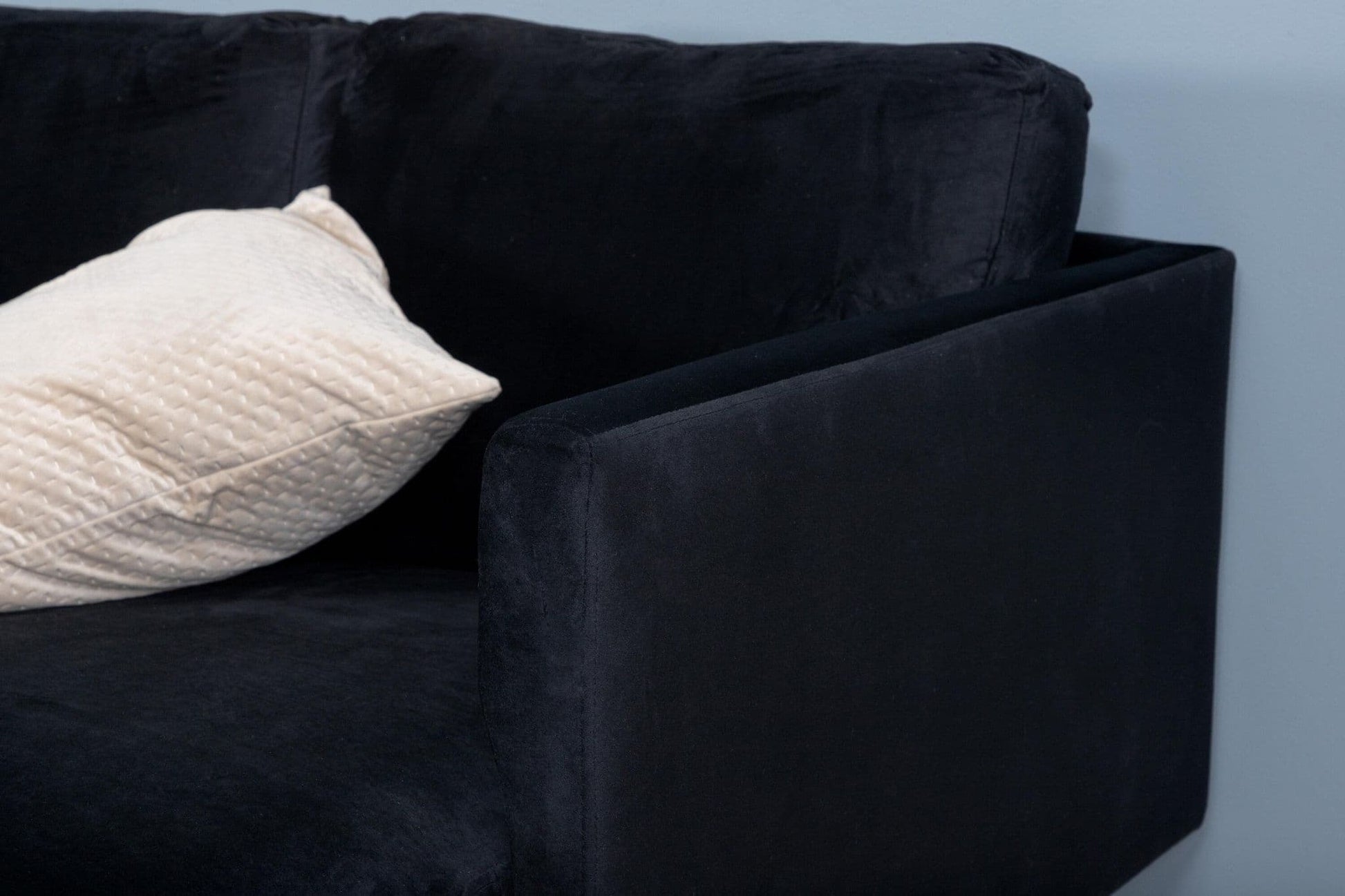 Black sofa with a white pillow against a light blue wall