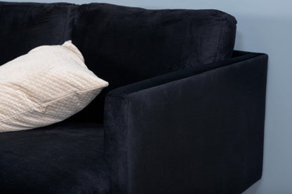 Black sofa with a white pillow against a light blue wall