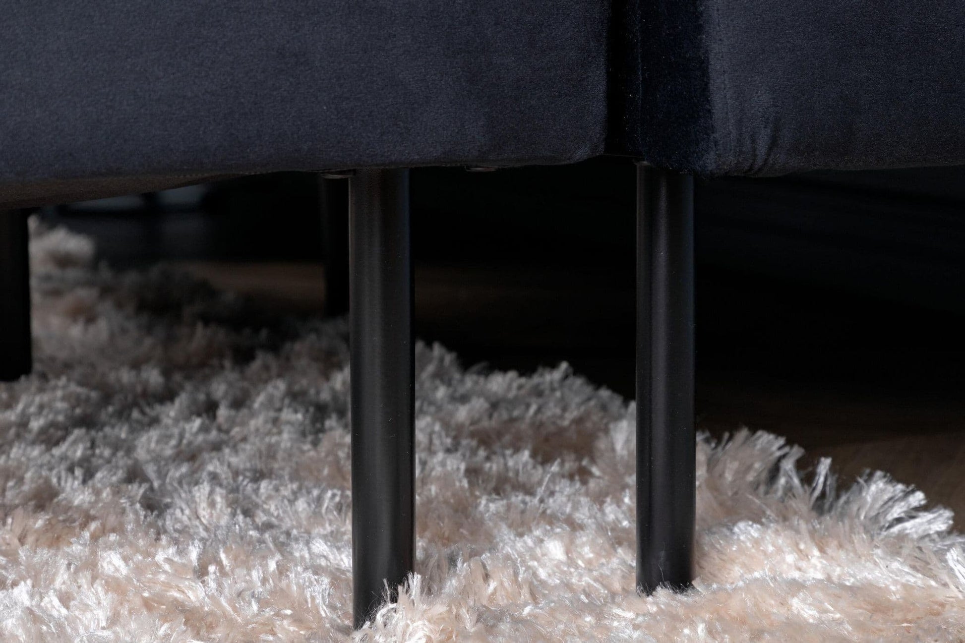 Close-up of a dark gray sofa with metal legs on a textured beige carpet.