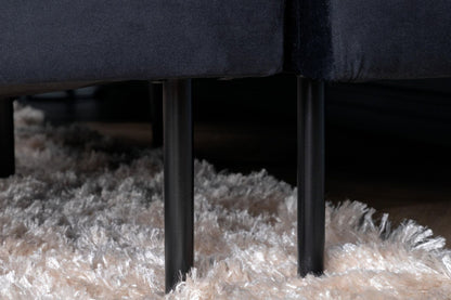 Close-up of a dark gray sofa with metal legs on a textured beige carpet.